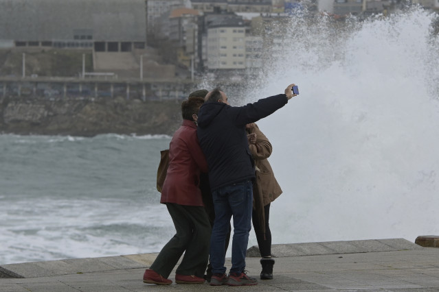Un grupo de persoas faise unha fotografía na zona das Escravas, ao 8 de decembro de 2021, na Coruña, Galicia, (España). A borrasca Barra fixo que a Xunta haxa activado para todo o litoral galego unha alerta laranxa por temporal costeiro. S