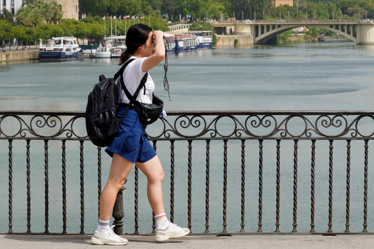 Una persona paseando por el Puente de Triana se protege la cara el día en que la capital está en alerta naranja por el calor , a 19 de julio del 2023.