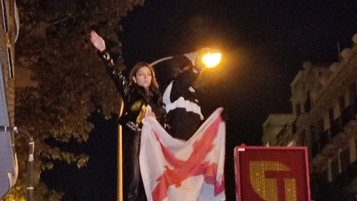 Una de las participantes en la manifestación frente a la sede del PSOE subida a un kiosko realizando el saludo fascista