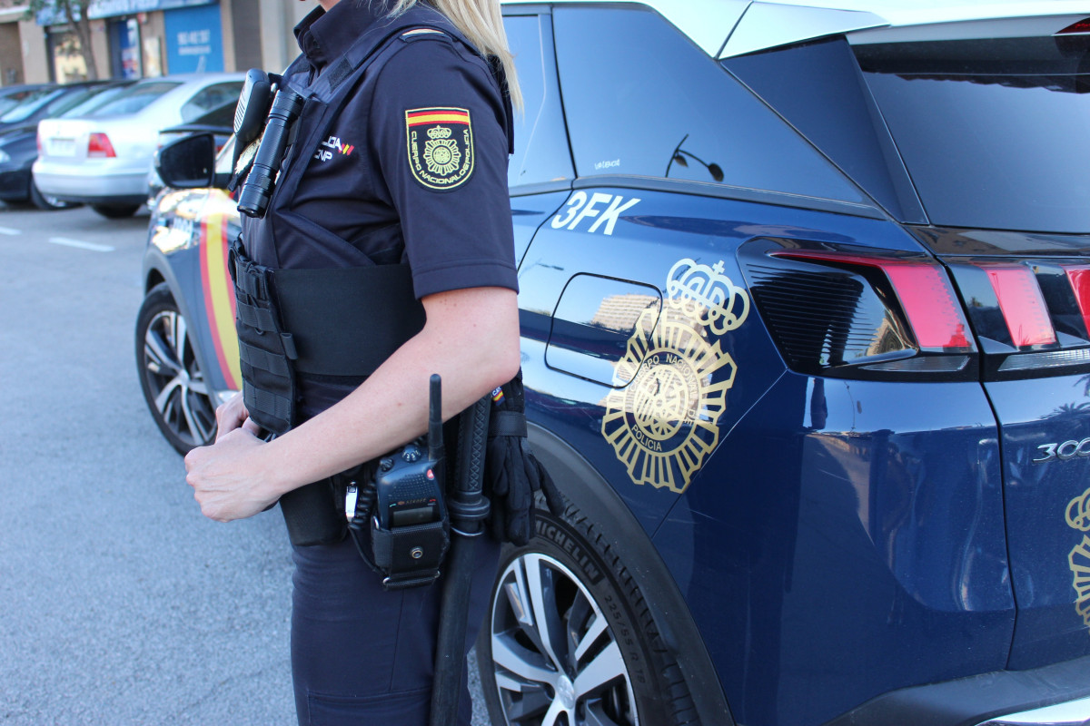 Imagen de una agente y de un coche patrulla de la Policía Nacional.