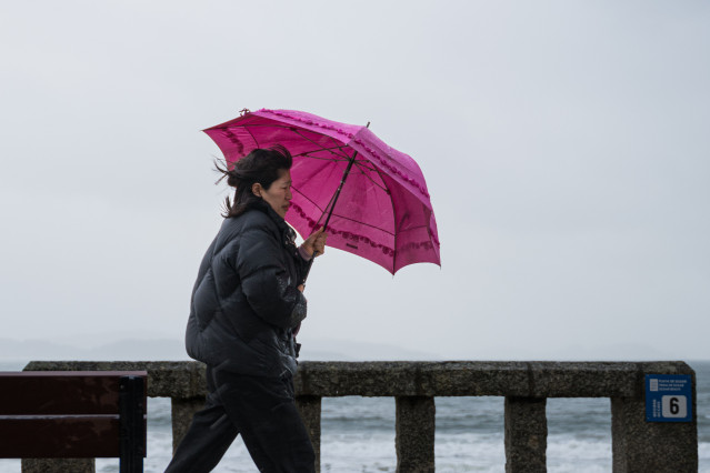 Archivo - Una mujer se refugia de la lluvia con paraguas en la comarca de O Salnés.