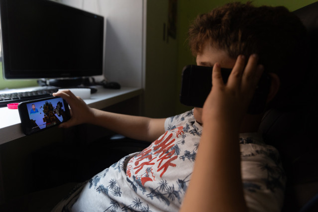 Archivo - Un niño usa el teléfono móvil y una tablet,