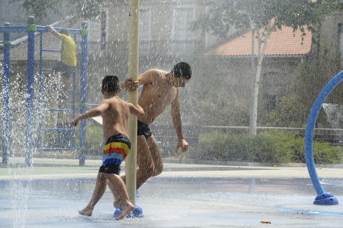 Dos personas se refrescan en unos chorros durante  la ola de calor.
