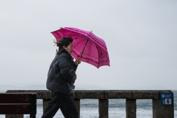 Archivo - Una mujer se refugia de la lluvia con paraguas.