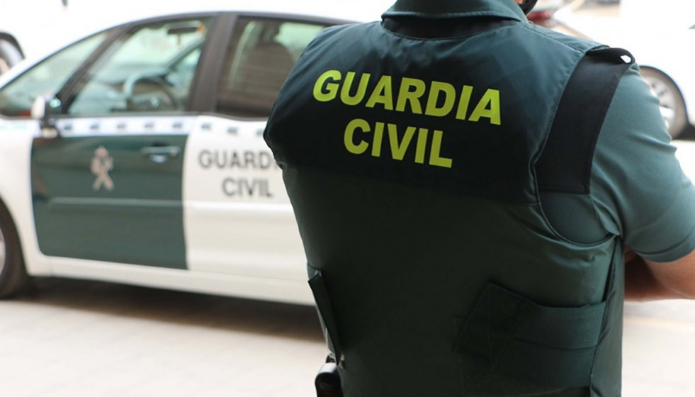 Archivo - Un agente de la Guardia Civil, de espaldas, junto a un vehículo oficial.