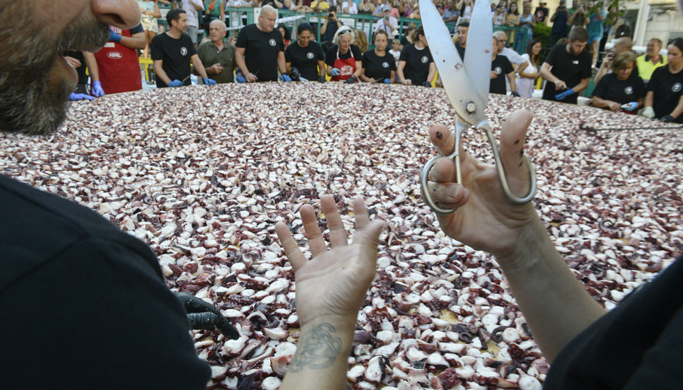 Archivo - Una persona sostiene unas tijeras frente a kilos de pulpo troceado en O Carballiño.