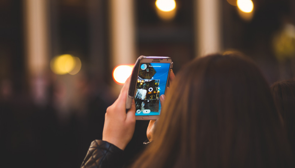 Archivo - Una chica mira la pantalla de su teléfono móvil.