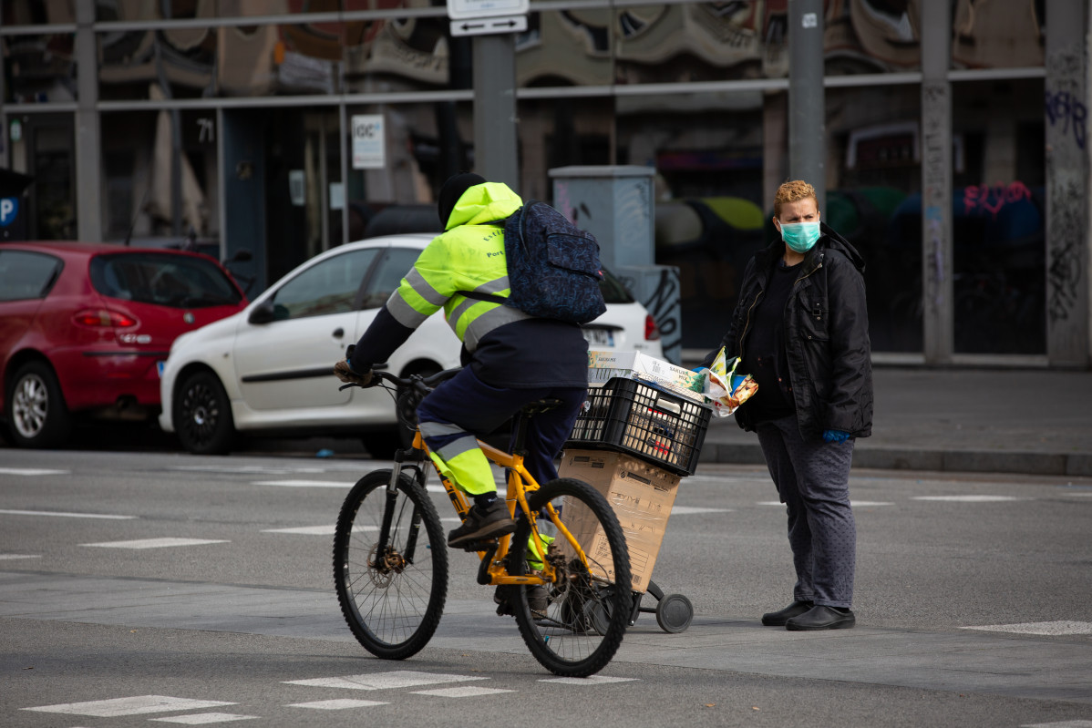 Un home que monta en bicicleta pasa xunto a unha muller protexida cunha máscara durante o noveno día laborable desde que se decretou o estado de alarma no país como consecuencia do coronavirus, en Barcelona/Catalunya (España) ao 26 de marzo de 2020.