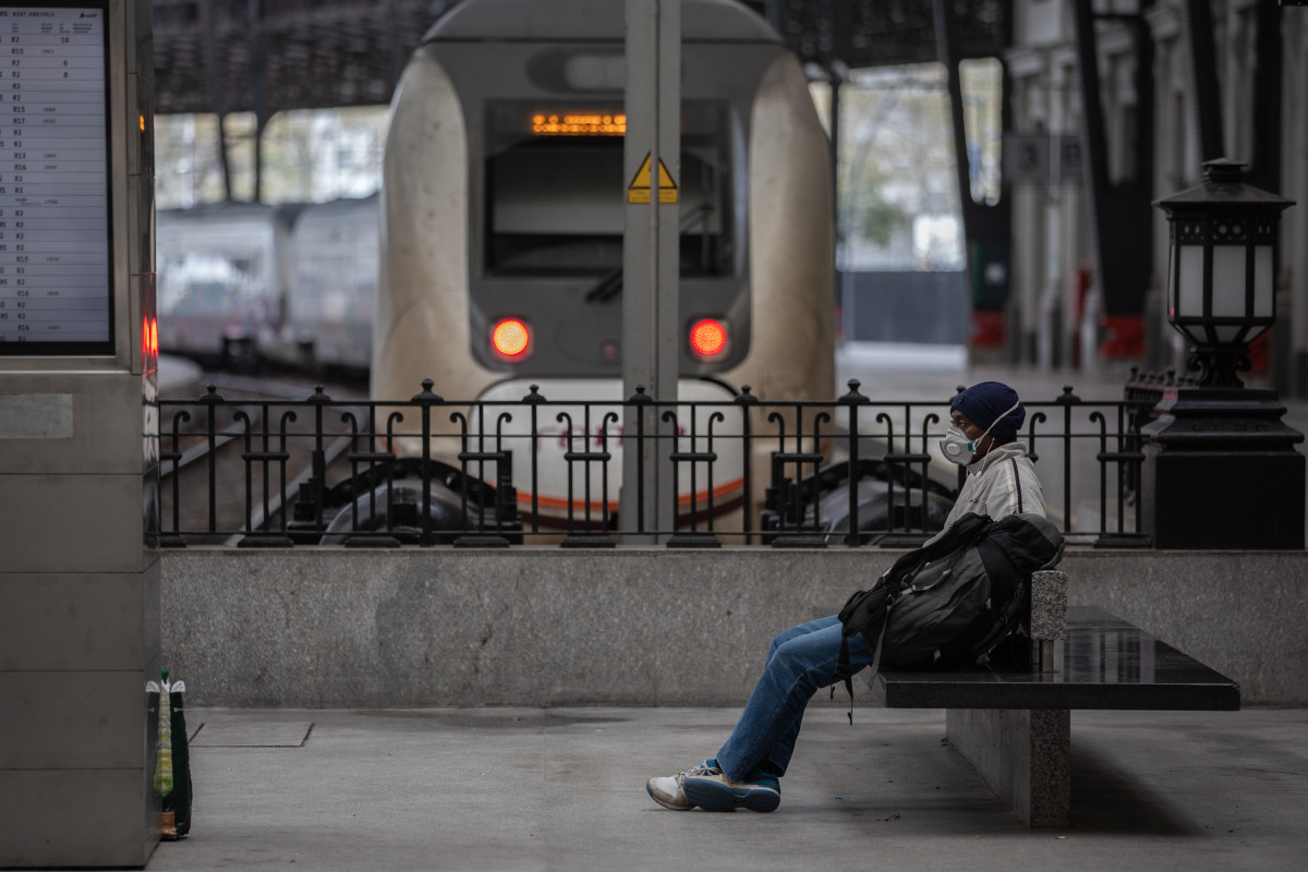 Un home protexido cunha máscara espera sentado nun banco nunha estación de tren de Barcelona durante o segundo día laborable do estado de alarma polo coronavirus, en Barcelona (España), ao 17 de marzo de 2020.