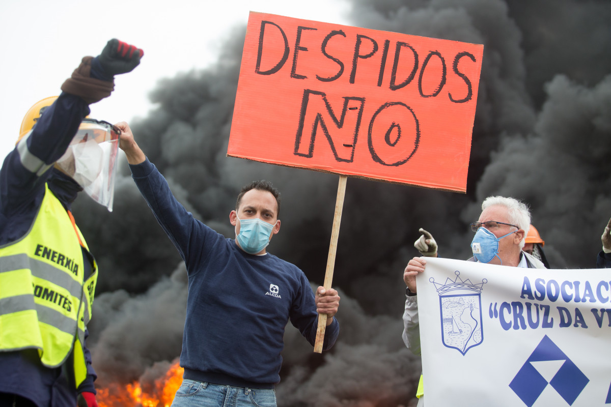 Un participante da manifestación do comité de empresa de Alcoa leva un cartel no que se le 'Despedimentos non' xunto á queima duns pneumáticos tras o anuncio hai tres días do despedimento. En