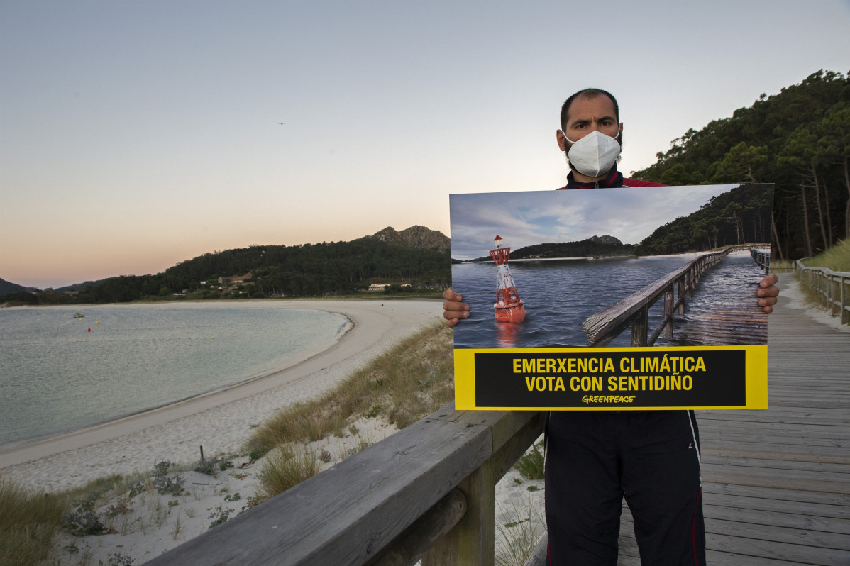 Un voluntario de Greenpeace porta unha fotografía modificada da Praia de Rodas, nas Illas Cíes, para simular os efectos da subida do nivel do mar.