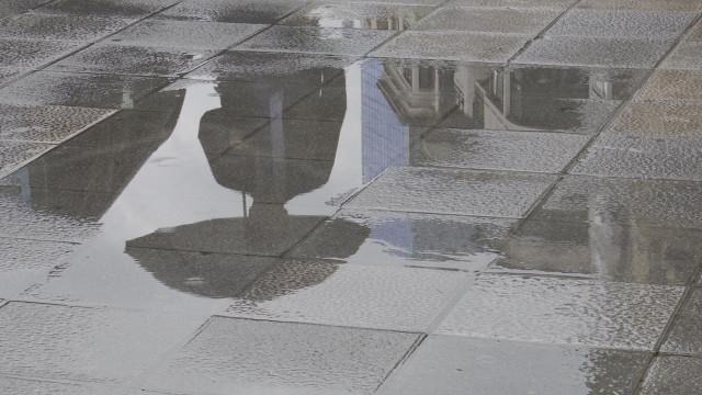 Unha persoa con paraugas reflíctese nun charco provocado pola choiva esta mañá en Bilbao.