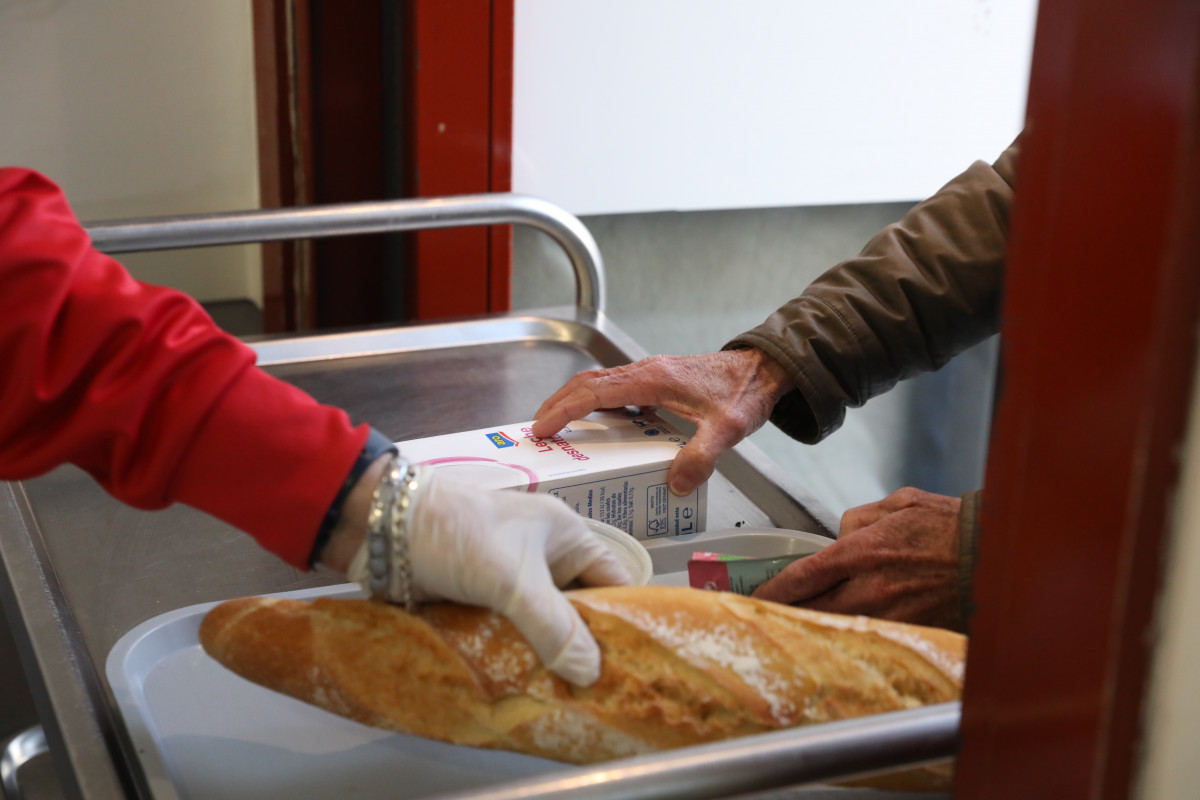 Un voluntario (i) trae comida a unha persoa (d) como parte da repartición diaria de alimentos do Comedor Social San José, en Puente de Vallecas, Madrid (España), ao 5 de febreiro de 2021.