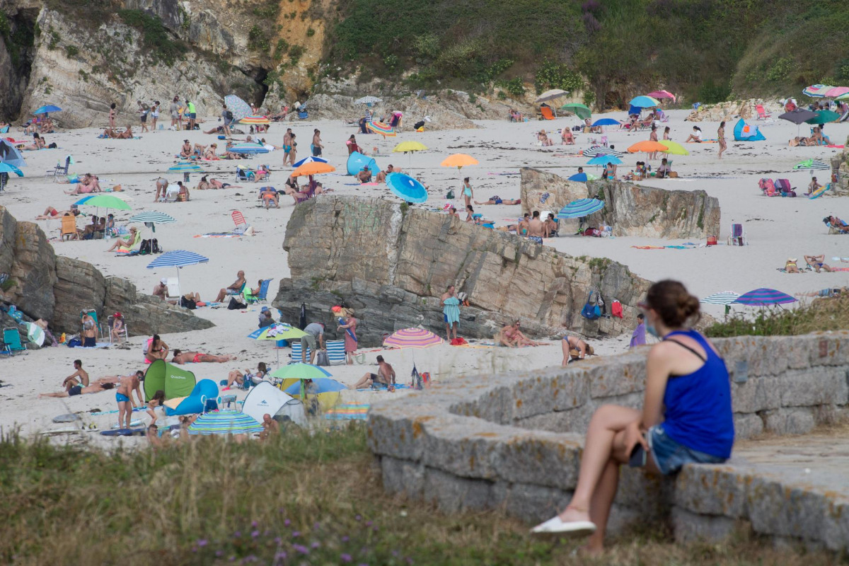 Arquivo - Unha persoa sentada fronte á praia na Mariña en xullo de 2020.