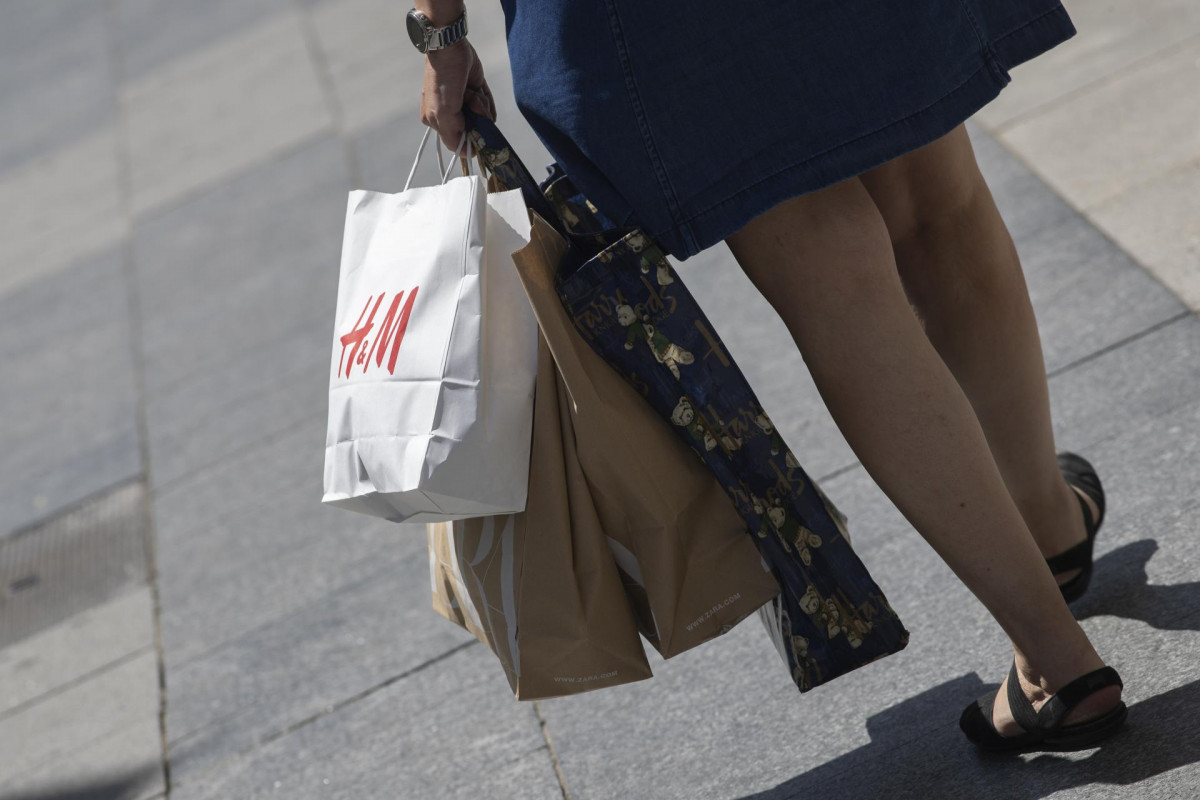 Archivo - Una mujer pasea cargada con varias bolsas, una de ellas perteneciente a la tienda H&M, durante el segundo día de rebajas, en Madrid (España), a 26 de junio de 2020. La cadena textil sueca