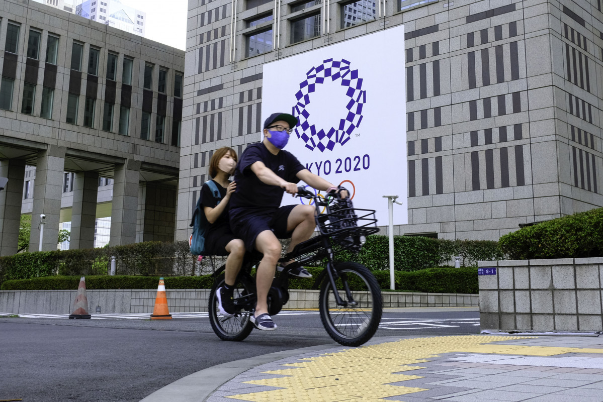 Unha parella pasea en bicicleta por diante do cartel dos Xogos Olímpicos de Tokyo 2020.