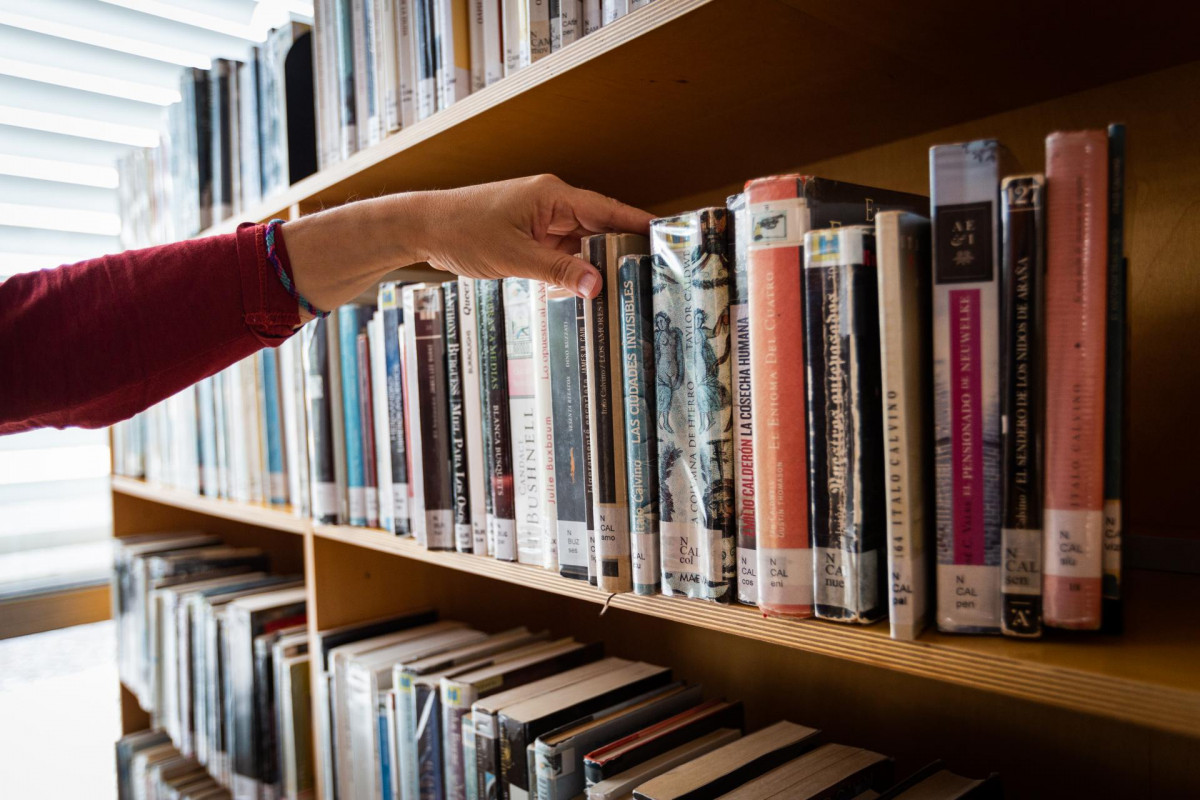 Archivo - Una bibliotecaria coge un libro de una estantería de la Biblioteca municipal del Centro Cívico Aldabe en Vitoria-Gasteiz tras su reapertura