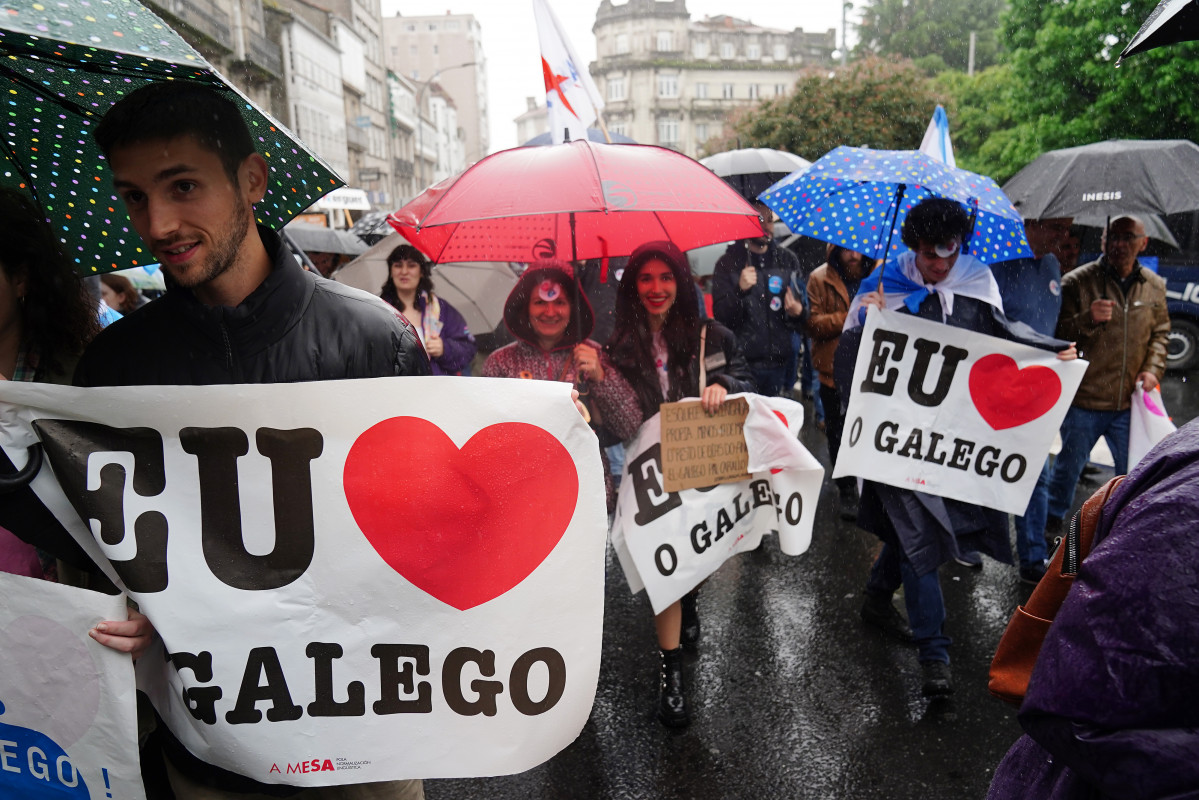 Varias persoas con paraugas e carteis nos que se le: 'Eu Ou Galego (falo galego)', participan nunha manifestación, baixo o lema: ‘Queremos Galego’, ao 17 de maio de 2022, en Santiago de Co