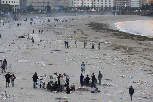 Vista xeral da praia de Orzán con grupos de persoas e restos de lixo despois da celebración das fogueiras da noite de San Juan.