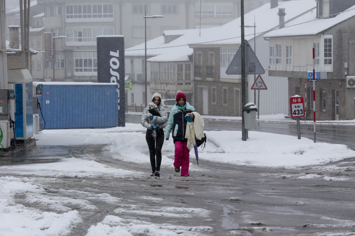 Dos mujeres caminan con su perro por una calle cubierta de nieve, a 26 de enero de 2023, en Pedrafita do Cebreiro, Lugo, Galicia.