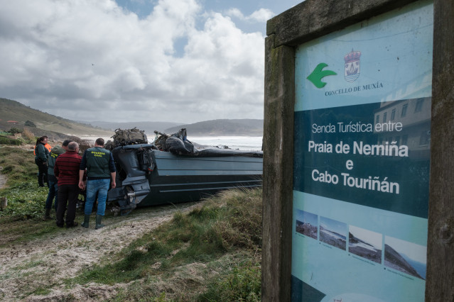 Miembros de la Guardia Civil observan el interior de la planeadora varada en la playa de Nemiña, a 24 de marzo de 2023, en Muxía, A Coruña, Galicia (España). La planeadora varada en la playa de Nemiña, en el municipio coruñés de Muxía, permanece boca abaj