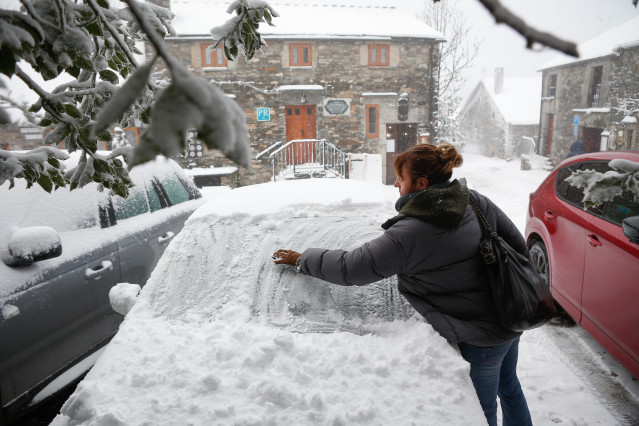 Una mujer limpia la nieve de su coche, a 9 de diciembre de 2024, en Pedrafita do Cebreiro, Lugo, Galicia (España). Un total de 12 comunidades autónomas están hoy en riesgo (alerta amarilla) por nieve, lluvias, oleaje y fuertes rachas de viento, en especia