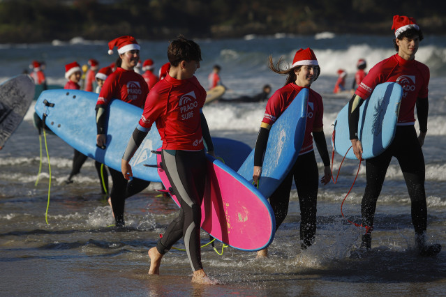 Decenas de personas disfrazadas de Papá Noel surfean durante la Papanoelada Surfera, en la playa de Patos.